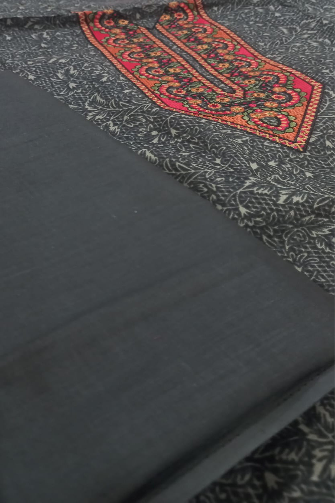 Black fabric with a red and gold embroidered design on a textured surface