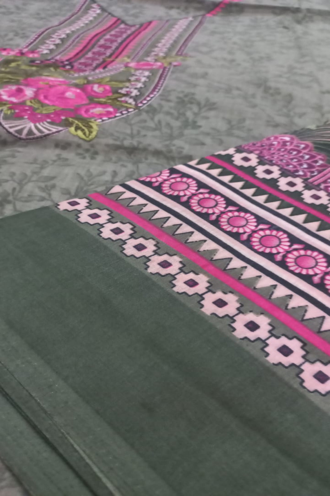 Traditional embroidered fabric with pink and green patterns on a gray background