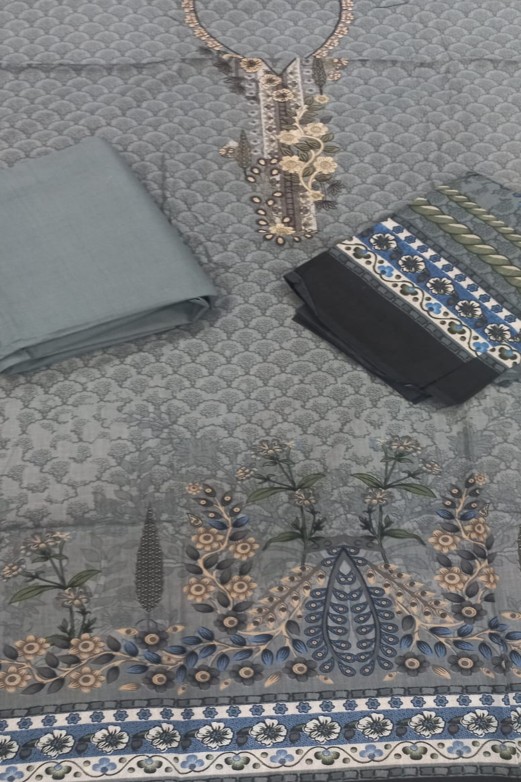 Decorative fabric with embroidery, a necklace, and a wallet on a textured surface.